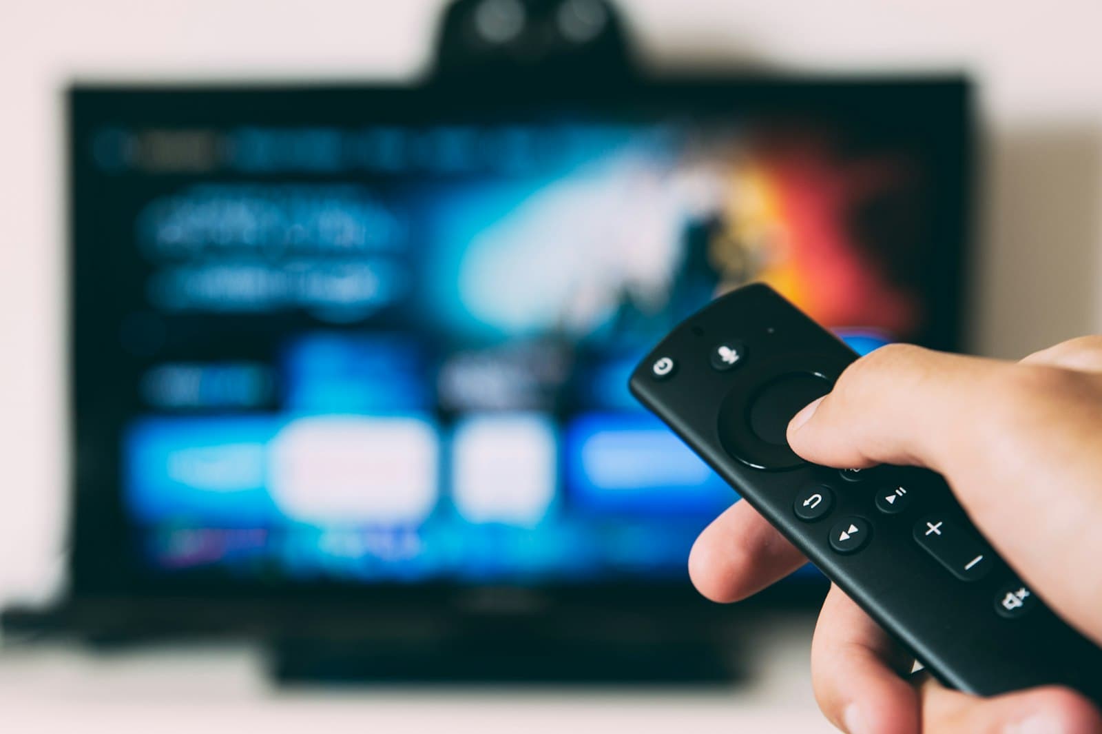 Hand holding a streaming device remote in front of a TV